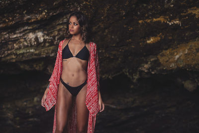 Young woman wearing bikini with shrug while standing against rock formations