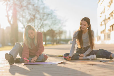 Smiling females writing on posters while sitting on street