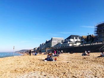 People on beach against clear blue sky