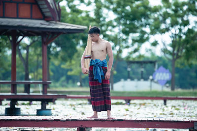 Full length of shirtless woman standing against trees