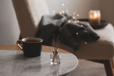 Bamboo sticks in bottle with scented candles and cup of tea on marble table closeup. home aroma. 