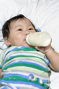 Baby girl drinking milk from milk bottle on bed at home