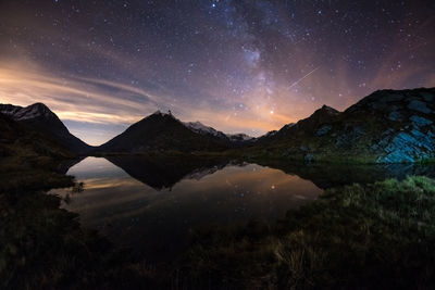 Scenic view of lake by mountains against sky at night