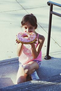 Girl eating large donut in city