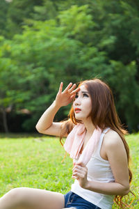 Woman shielding eyes while sitting on field