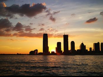 Silhouette buildings by sea against sky during sunset