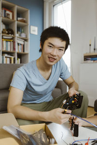 Portrait of smiling teenage boy holding machine part while making project at home