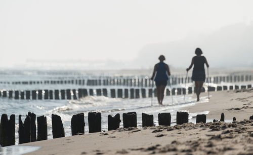 Rear view of women walking at beach against sky