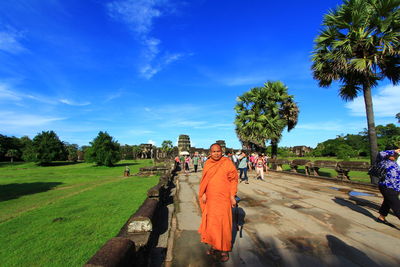 People on footpath by palm trees against blue sky