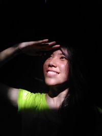 Portrait of smiling teenage girl shielding eyes while looking away in darkroom