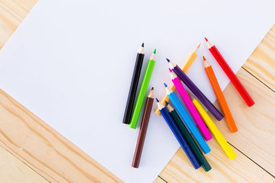 Directly above shot of colored pencils and paper on wooden table