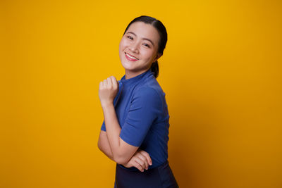 Portrait of smiling young woman against yellow background