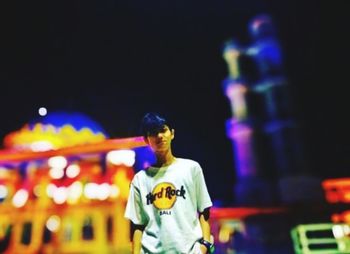 Portrait of young man with illuminated carousel in amusement park