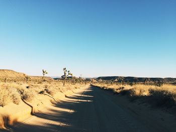 Dirt road in desert against clear sky