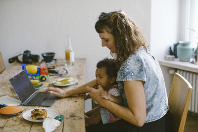 Woman using feeding food to daughter while sitting at dining table in house