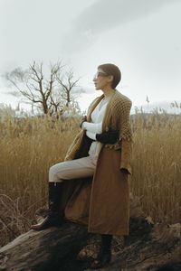 Young woman looking away while standing on field against sky