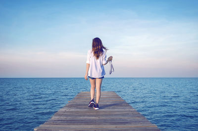 Rear view of woman standing on beach against sky