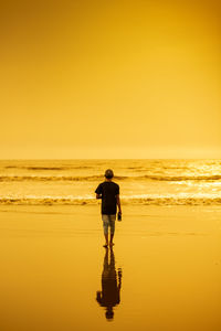 Rear view of man standing on beach during sunset