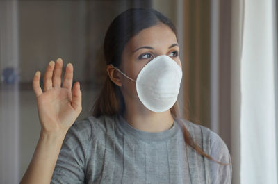 Young woman wearing flu mask looking away standing at home