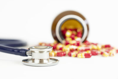 Close-up of capsules spilling from bottle by stethoscope against white background