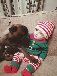 Full length of baby boy in knit hat with dog relaxing on sofa at home