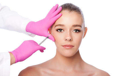 Cropped hands of surgeon giving botox injection to woman against white background