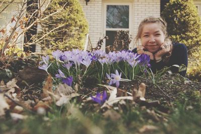 Portrait of smiling young woman lying by flowering plants on land