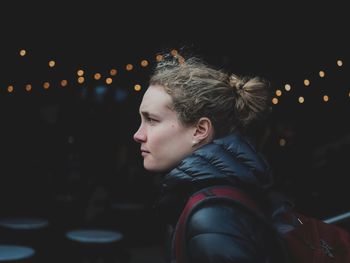 Young woman looking away while standing against illuminated lights