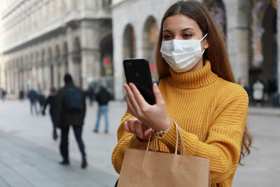 Woman wearing mask video calling on phone standing outdoors