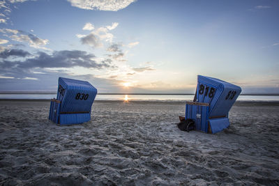 Hooded chairs at beach against sky during sunset