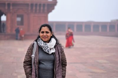 Portrait of young woman standing against building