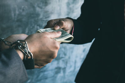 Cropped hands of business people holding money against wall