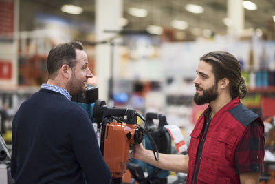 Salesman discussing over machinery with male customer in hardware store