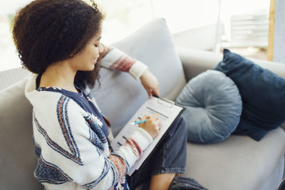 Young woman using phone while sitting on sofa at home