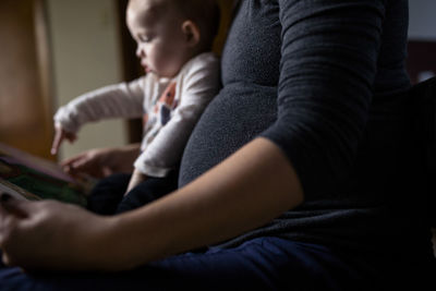 Midsection of pregnant woman showing picture book to daughter while sitting at home