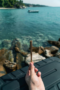 Cropped hand holding marijuana joint against sea