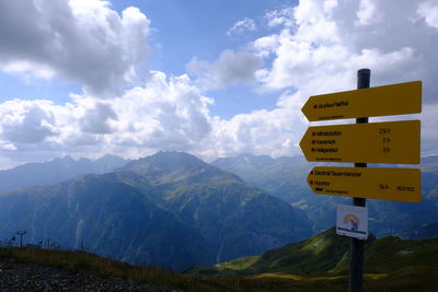 Road sign by mountains against sky