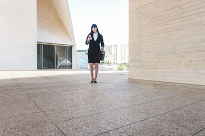 Full length of young woman standing against building