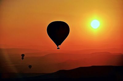 Silhouette hot air balloon flying against orange sky