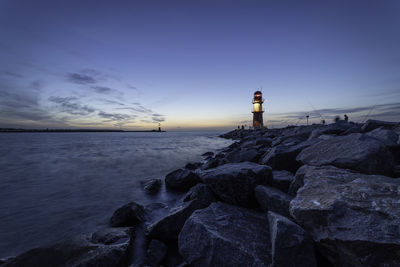 Lighthouse on rocks by sea against sky