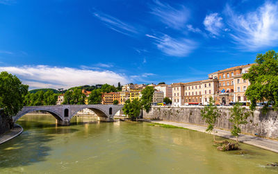 Bridge over river by buildings against blue sky