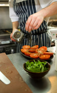 Chef sprinkles herbs on tomatoes in restaurant kitchen