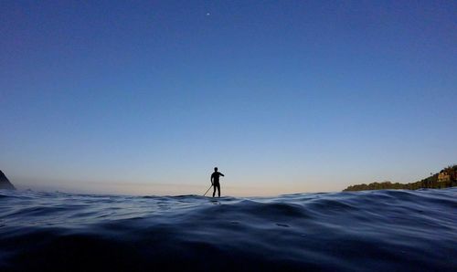 Silhouette man on beach against clear blue sky