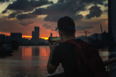 Rear view of man photographing sunset over city at kowloon bay