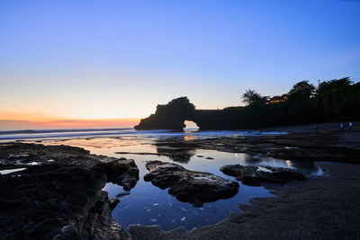 Rocks on beach against sky during sunset