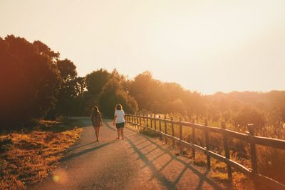 Rear view of girls walking on road amidst trees against clear sky