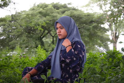 Young woman looking away while standing on land against trees