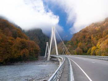 Bridge over road amidst trees against sky during autumn