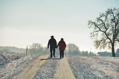 Rear view of men walking on snow covered field