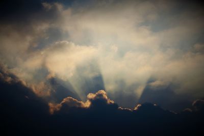 Low angle view of sunlight streaming through clouds